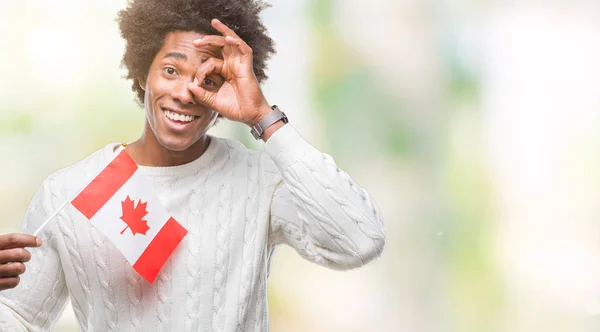 アフロ アメリカ人が指を通して見る目に手で サインをして笑っている幸せそうな顔で孤立した背景にカナダのフラグします — ストック写真