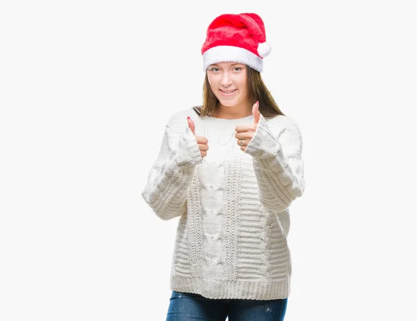若い美しい白人女性のハッピー サムズアップ手でジェスチャーをして孤立した背景にクリスマス帽子をかぶっています 成功を示すと カメラを見て式を承認します — ストック写真