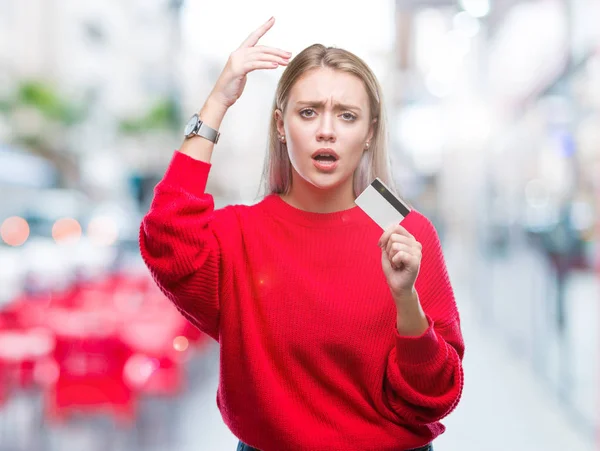 Young blonde woman holding credit card over isolated background annoyed and frustrated shouting with anger, crazy and yelling with raised hand, anger concept