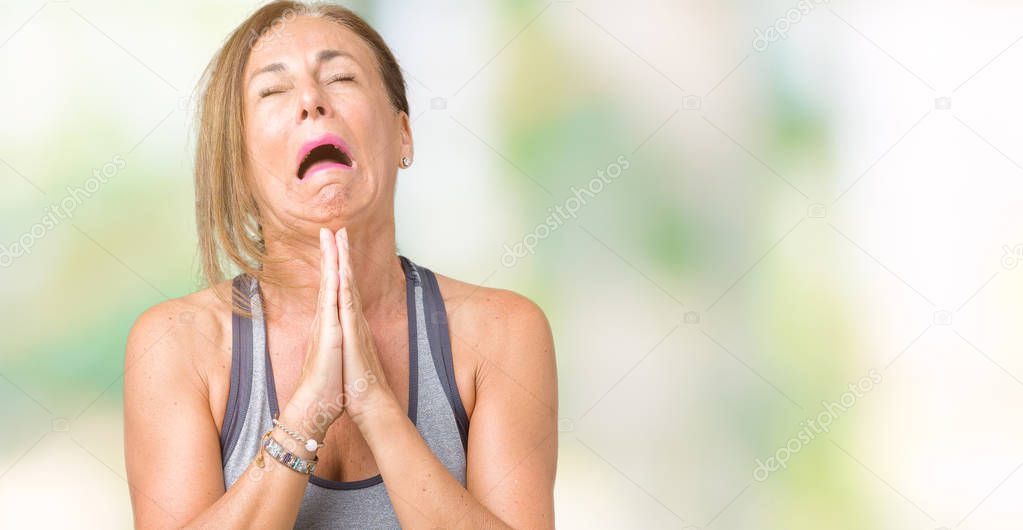 Beautiful middle age woman wearing sport clothes over isolated background begging and praying with hands together with hope expression on face very emotional and worried. Asking for forgiveness. Religion concept.