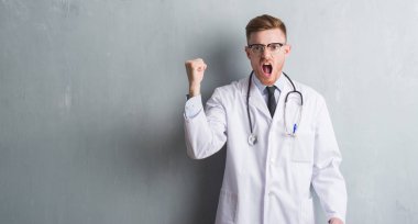 Genç redhead Doktor adam gri grunge Duvar ile öfke, çılgın ve yükseltilmiş eliyle diye bağıran rahatsız ve hayal kırıklığına uğramış öfke kavramı bağırarak