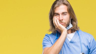 Genç yakışıklı Doktor adam uzun saçlı izole arka plan düşünme seyir üzerinde yorgun ve sıkılmış çapraz silah depresyon sorunları ile.