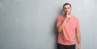 Beyaz delikanlı dudaklarında parmak ile sessiz olmanı gri grunge duvarın üzerinden. Sessizlik ve gizli kavramı.