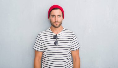Yakışıklı genç hipster adam yüzünde lacivert t-shirt ve ciddi ifade ile yün kap giyen gri grunge duvarın üzerinden. Basit ve doğal kameraya bakıyor.
