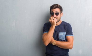 Yakışıklı genç adam stresli ve gergin elle çivi ısırma ağzına bakarak güneş gözlüğü takıyor gri grunge duvarın üzerinden. Anksiyete sorunu.