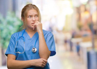 Stresli ve gergin elle çivi ısırma ağzına bakarak izole arka plan üzerinde cerrah üniforma giyen genç beyaz doktor kadın. Anksiyete sorunu.