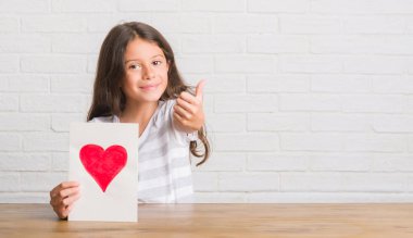 Anneler günü vererek masada oturan genç İspanyol çocuğun ok işareti yapıyor büyük gülümseme ile mutlu kartı, parmaklarıyla, mükemmel işaret parmak