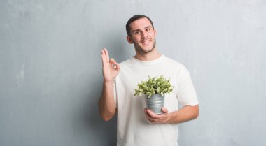 Parmak, mükemmel sembolü ile ok işareti yapıyor bitki pot tutan gri grunge duvarın üzerinden beyaz delikanlı