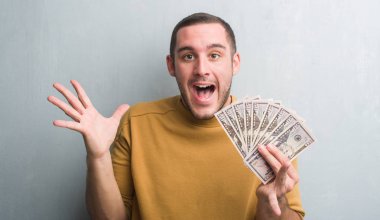 Dolar çok mutlu ve heyecanlı, kazanan ifade ile çığlık zaferini kutluyor büyük holding gri grunge duvarın üzerinden beyaz delikanlı gülümse ve el kaldırdı