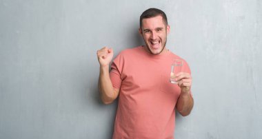 Duygu tezahürat Genç beyaz adam gurur çığlık ve zafer ve başarı çok heyecanlı, kutlama su içme gri grunge duvarın üzerinden