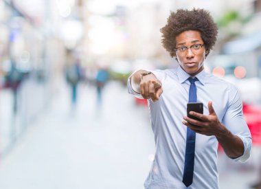Afro Amerikan iş adamı manifatura üzerinden Smartphone kullanarak kamera ve size parmak ile işaret arka plan izole, el işareti, pozitif ve kendinden emin bir jest ön