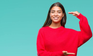 Üzerinde kış kazak giyen genç güzel Arap kadın arka plan ile büyük ve büyük boy işaret, ölçü birimi sembol gösteren el eller izole. Kameraya bakarak gülümsüyordu. Ölçüm kavramı.