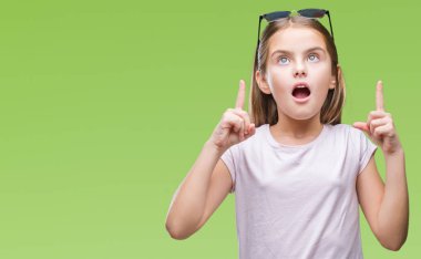 Genç güzel kız hayran ve yukarıya bakıyor ve parmakları ile işaret ve silah kaldırdı sürpriz izole arka plan üzerinde güneş gözlüğü takıyor.