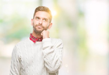 Çene düşünme hakkında soru, dalgın ifade üzerine el ile izole arka plan üzerinde kış kazak giyen genç yakışıklı adam. Düşünceli yüzüyle gülümsüyor. Şüphe kavramı.