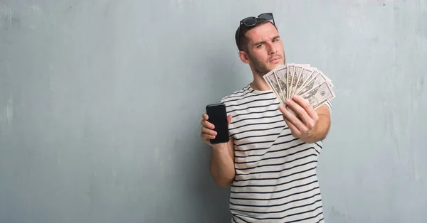 Joven Hombre Caucásico Sobre Pared Gris Grunge Sosteniendo Dólares Teléfono — Foto de Stock