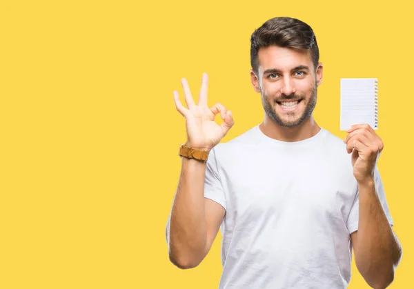 Joven Hombre Guapo Sosteniendo Cuaderno Sobre Fondo Aislado Haciendo Signo — Foto de Stock