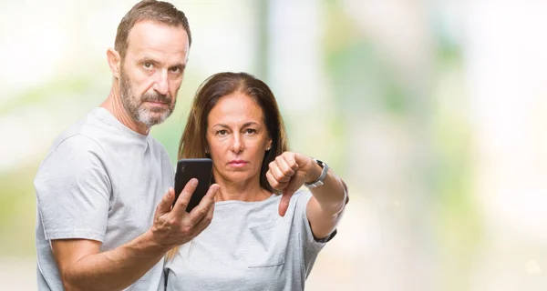 中年西班牙夫妇在智能手机上的短信与愤怒的脸隔离的背景 显示不喜欢大拇指的负号 拒绝的概念 — 图库照片