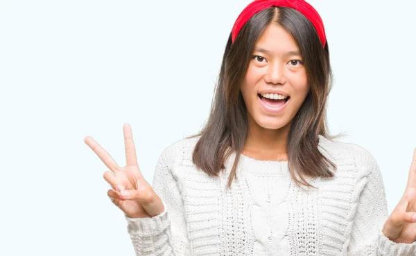 年轻的亚洲妇女穿着冬季毛衣在孤立的背景微笑着快乐的脸眨眼在相机做胜利标志 第二个 — 图库照片