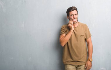 Diş ağrısı veya dişlerde dişlerle ilgili hastalık nedeniyle ağız acı ifadesi ile el ile dokunmak gri grunge duvarın üzerinden yakışıklı genç adam. Diş hekimi kavramı.