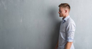 Genç redhead iş adamı tarafına, seyir gri grunge duvarın üzerinden dinlenmek doğal yüz emin gülümseme ile pozuyla profili.