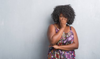 Gri grunge duvar renkli giyen genç Afro-Amerikan kadın stresli ve gergin elle çivi ısırma ağzına elbise arıyorum. Anksiyete sorunu.