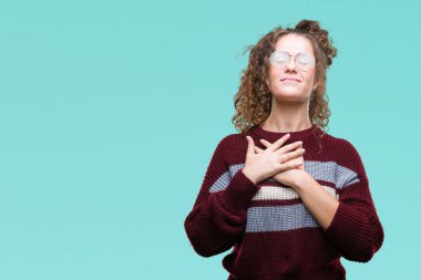 Güzel esmer kıvırcık saçlı Genç kız göğüs kapalı gözlerle ellerinde ve yüzünde minnettar jest ile gülümseyen izole arka plan üzerinde gözlük takıyorum. Sağlık kavramı.