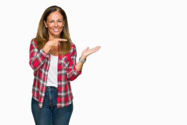 Hayret ve el ile sunulması ve parmak ile işaret ederken kameraya gülümseyen izole arka plan üzerinde rahat forması giyen orta yaş yetişkin kadın.