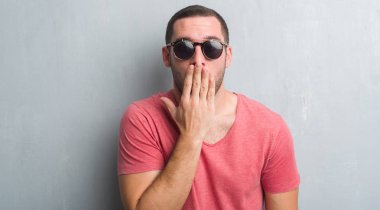 Güneş gözlüğü kapak ağız elle hata, korku, sessizlik içinde gizli kavramı korkmuş ifade için utanç ile şok giyen gri grunge duvarın üzerinden beyaz delikanlı