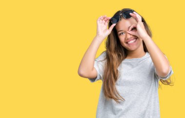 Genç güzel esmer kadın gülümsüyor, parmakları ile mutlu yüz üzerinden seyir göz el ile ok jest yapıyor izole arka plan üzerinde güneş gözlüğü takıyor.