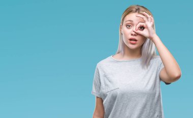 Sürpriz yüz, göz parmaklarının arasından seyir ile ok jest yapıyor izole arka plan üzerinde sarışın genç kadın şok. İmansız ifade.