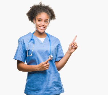 Genç afro Amerikalı doktor kadın gülümseyerek ve iki elleri ve parmakları ile tarafına işaret kamera bakarak izole arka plan.