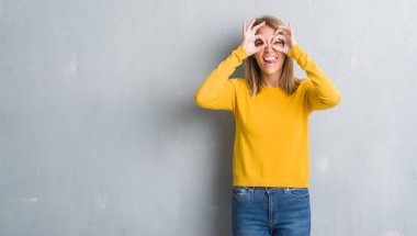 Dilini, parmaklarının arasından baktığını yapışmasını dürbün gibi ok jest yapıyor grunge gri duvar üzerinde duran güzel genç kadın. Deli ifade.