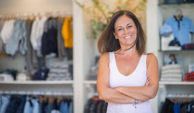 Güzel orta yaş İspanyol kadın giyim mağazasında yüzünde gülümseme ile ayakta. Dükkan sahibi ve tezgâhtar kendinden emin ve neşeli çapraz silah ile gülümseyen.