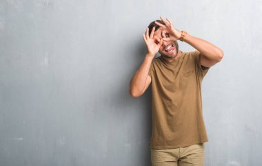 Yakışıklı delikanlı, dilini parmaklarının arasından baktığını yapışmasını dürbün gibi ok jest yapıyor gri grunge duvarın üzerinden. Deli ifade.