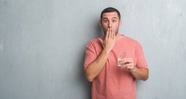 Hata, korku, sessizlik içinde gizli kavramı korkmuş ifade için utanç ile su kapak ağız el ile bir bardak içme gri grunge duvarın üzerinden beyaz delikanlı şok