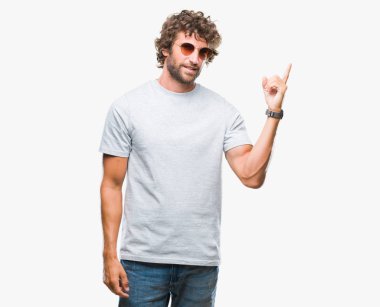 Yüzünde kocaman bir gülümseme ile izole arka plan üzerinde güneş gözlüğü takıyor yakışıklı İspanyol modeli adam kameraya bakarak yan el ve parmak ile işaret.