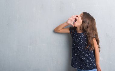 Genç İspanyol çocuk bağırarak ve ağzı üzerinde el ile yan için çığlık grunge gri duvar için. İletişim kavramı.