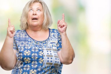 Kıdemli artı izole arka plan üzerinde beyaz kadın hayrete ve yukarıya bakıp parmakları ile işaret şaşırttı ve silah kaldırdı boyutu.