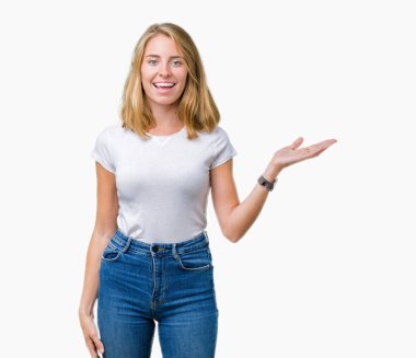 Neşeli sunulması ve kameraya bakarak avucunun ile işaret gülümseyen izole arka plan üzerinde rahat beyaz t-shirt giyen güzel genç kadın.