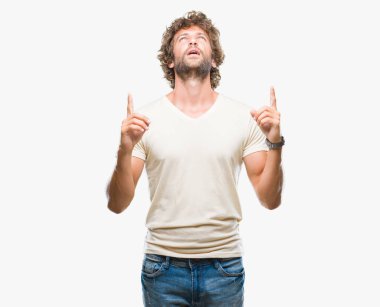 Handsome hispanic model man over isolated background amazed and surprised looking up and pointing with fingers and raised arms. clipart