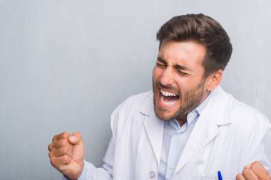 Yakışıklı genç profesyonel adam beyaz giyen gri grunge duvarın üzerinden kat çok mutlu ve heyecanlı kaldırdı kollarını açarak kazanan jest yapıyor, gülümseyen ve başarı için çığlık. Kutlama kavramı.