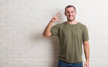 Beyaz tuğla duvar gülümseyen ve süre seyir ve kamera boyutu işaret parmaklarıyla yapıyor el ile kendinden emin eller üzerinde duran beyaz delikanlı. Ölçü kavramı.