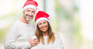 Orta yaş İspanyol çift üzerinde Noel şapka mutlu yüz ile gülümseyerek kameraya seyir silah geçti arka plan izole. Olumlu bir kişi.
