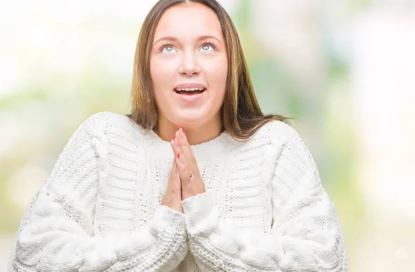 Young beautiful caucasian woman wearing winter sweater over isolated background begging and praying with hands together with hope expression on face very emotional and worried. Asking for forgiveness. Religion concept.