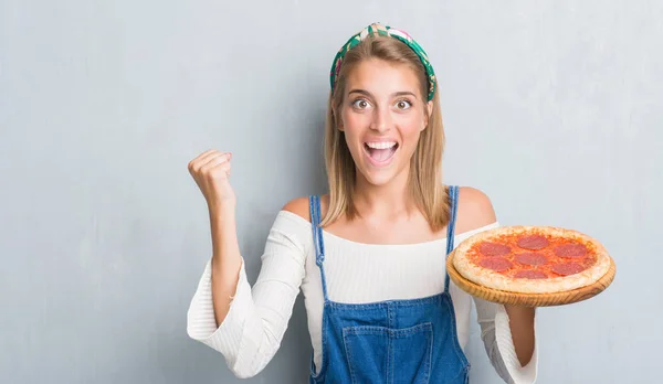 感情を応援して誇りに思って叫んでと勝利と非常に興奮して 成功を祝ってペパロニのピザを食べてグランジ灰色の壁に美しい若い女性 — ストック写真