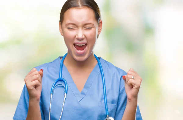 腕の成功のために興奮して孤立した背景に医療制服を着て若い白人医師女性は祝う勝利笑顔を発生します 勝者の概念 — ストック写真
