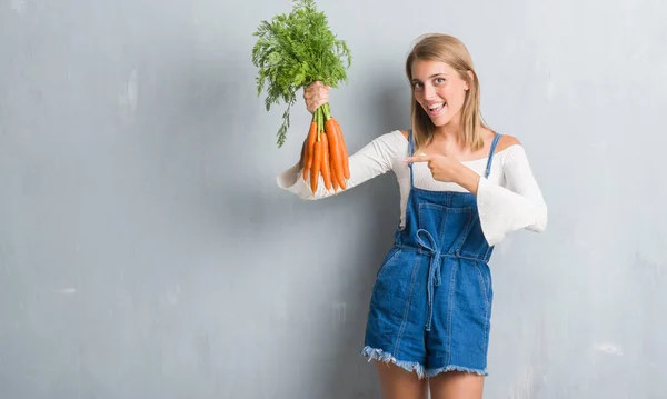 Vacker Ung Kvinna Över Grunge Grå Väggen Håller Färska Morötter — Stockfoto