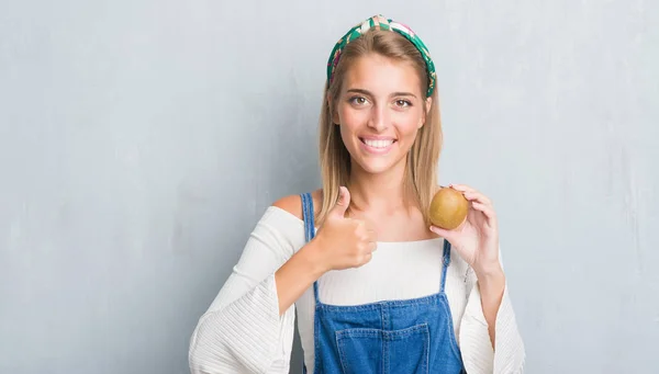 Vacker Ung Kvinna Över Grunge Grå Väggen Håller Färsk Kiwi — Stockfoto