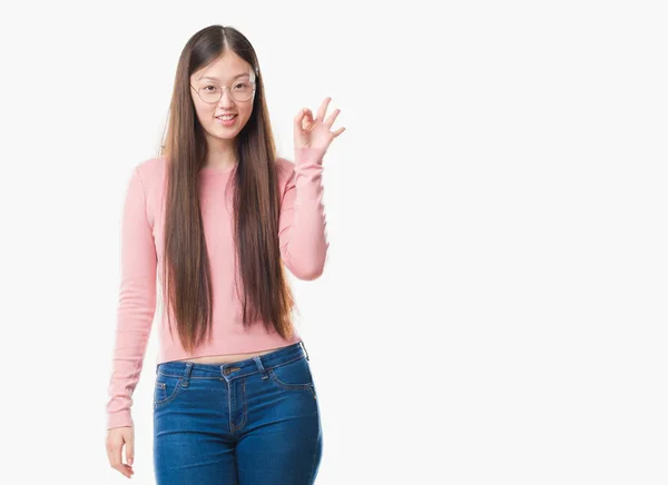 めがねを手と指で サインをしている肯定的な笑みを浮かべて孤立の背景の上の若い中国の女性 成功した式 — ストック写真