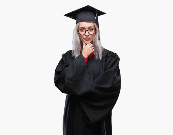 年轻的金发女子穿着毕业制服在孤立的背景下 看着自信的相机与交叉的手臂和手举起下巴 积极思考 — 图库照片